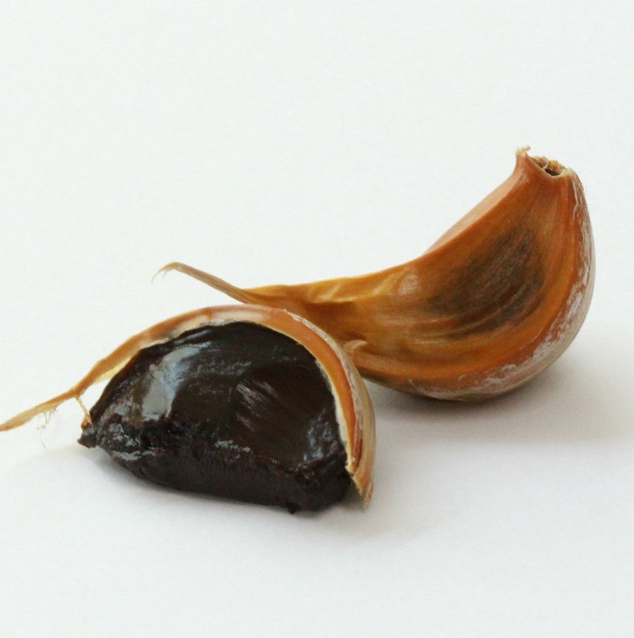 Black garlic clove with its papery skin opened to reveal the dark interior